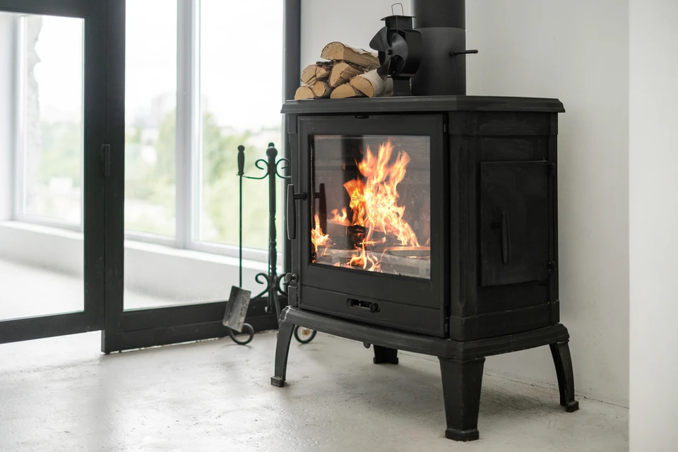 Intérieur moderne avec poêle à bois en fonte noire en fonctionnement, flammes visibles dans le foyer vitré