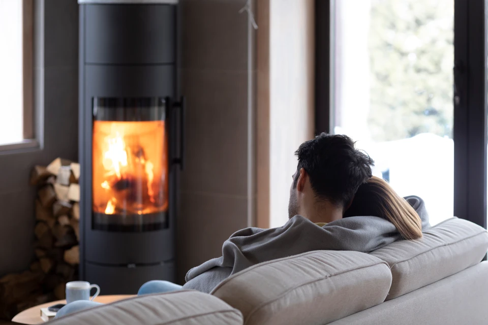 Une personne alimente un poêle à bois en fonctionnement, portant des gants de protection noirs pour insérer une bûche dans le foyer ouvert