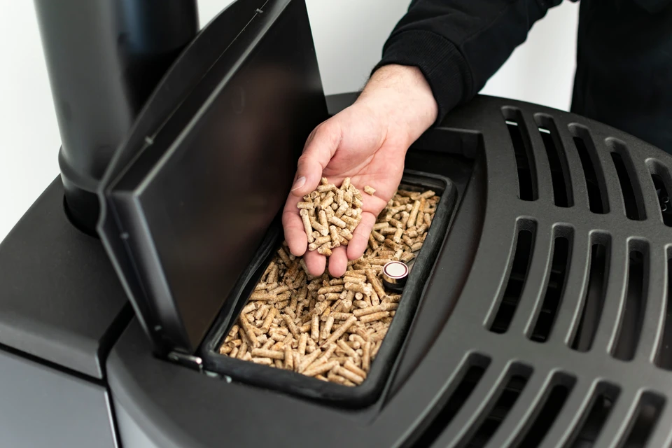 Une personne verse des granulés de bois dans un poêle à pellets domestique à l'aide d'un récipient rouge perforé